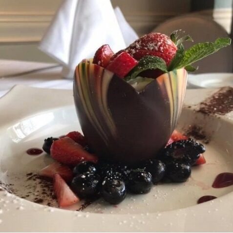 Elegant chocolate bowl filled with strawberries and mint on a white plate.